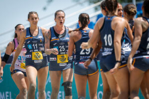 A group of athletes in matching blue uniforms walk together on a sandy court during a sports event.